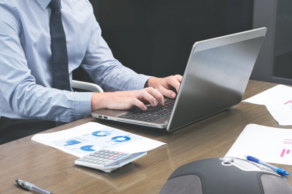 Person typing on a laptop at a desk with documents and charts beside it